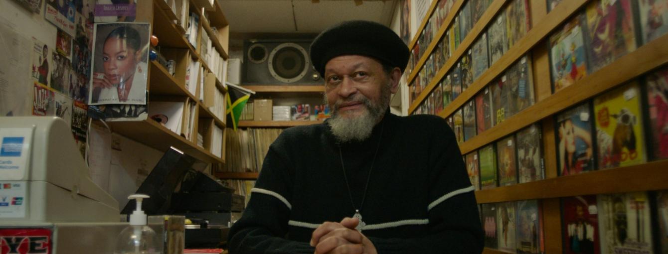 a record store owner sitting in his store surrounded by records