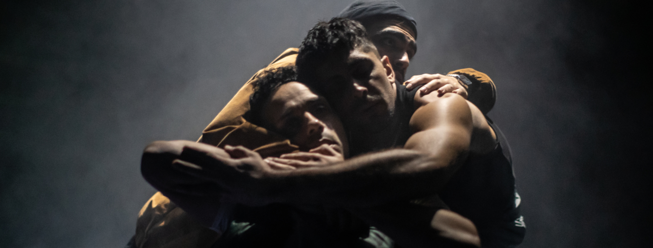 Three men embrace with their arms around each other. 