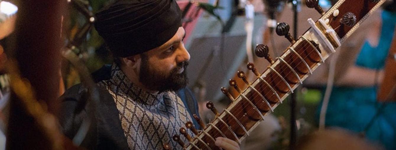 Opera North's poster for 'Orpheus'; A man wearing a turban with a sitar sits playing amongst a group of musicians.
